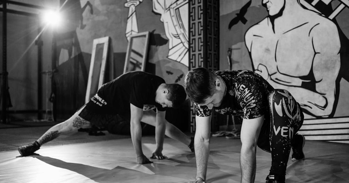 Two men stretching inside a gym, preparing for MMA training in a grayscale setting.