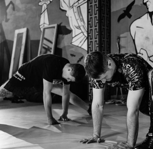 Two men stretching inside a gym, preparing for MMA training in a grayscale setting.