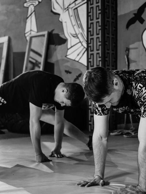 Two men stretching inside a gym, preparing for MMA training in a grayscale setting.