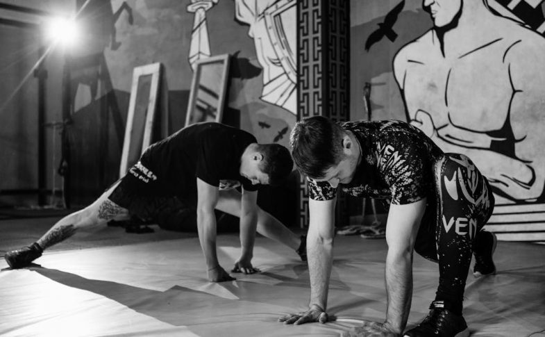 Two men stretching inside a gym, preparing for MMA training in a grayscale setting.